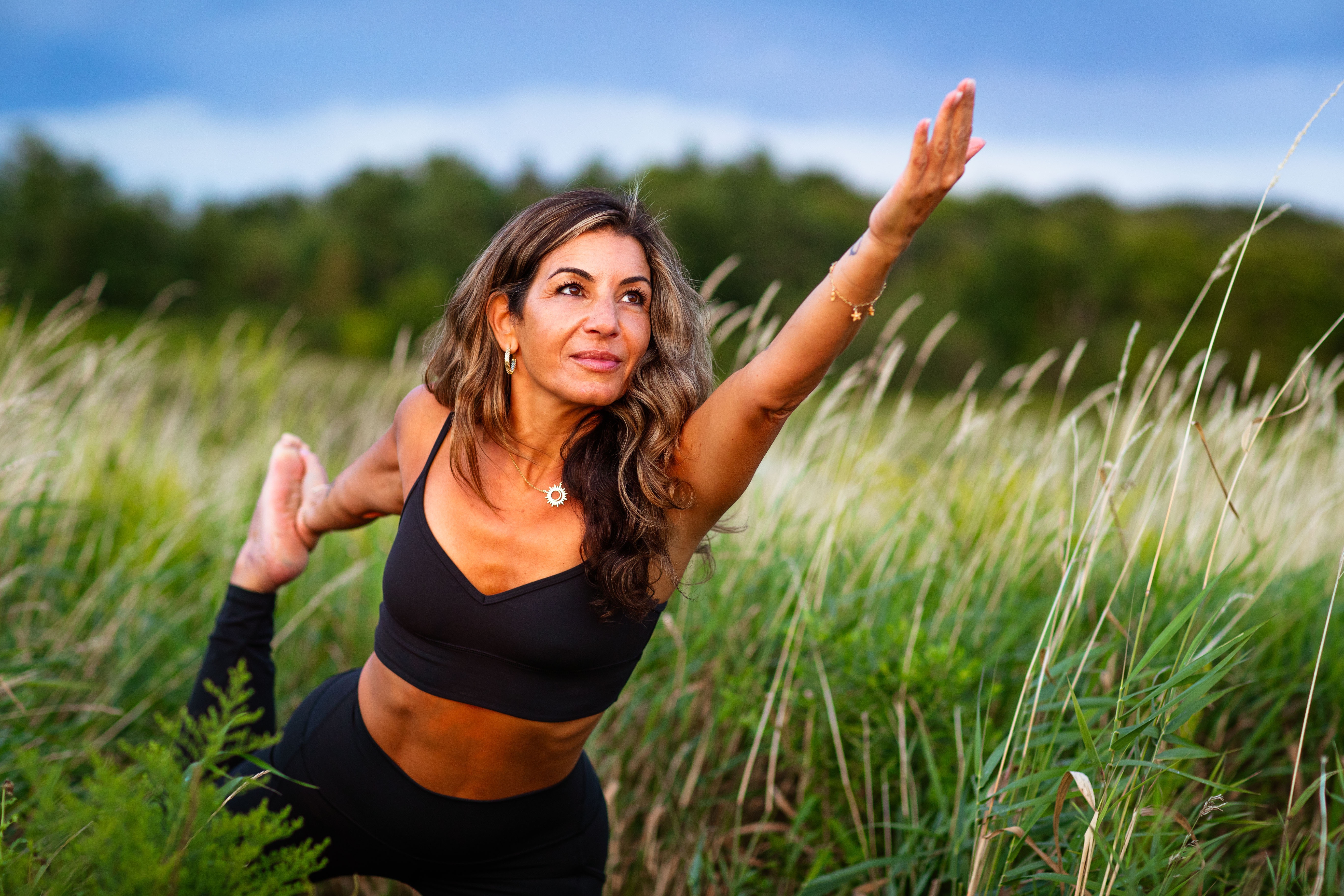 Adriana practicing a balancing yoga pose among coastal grasses